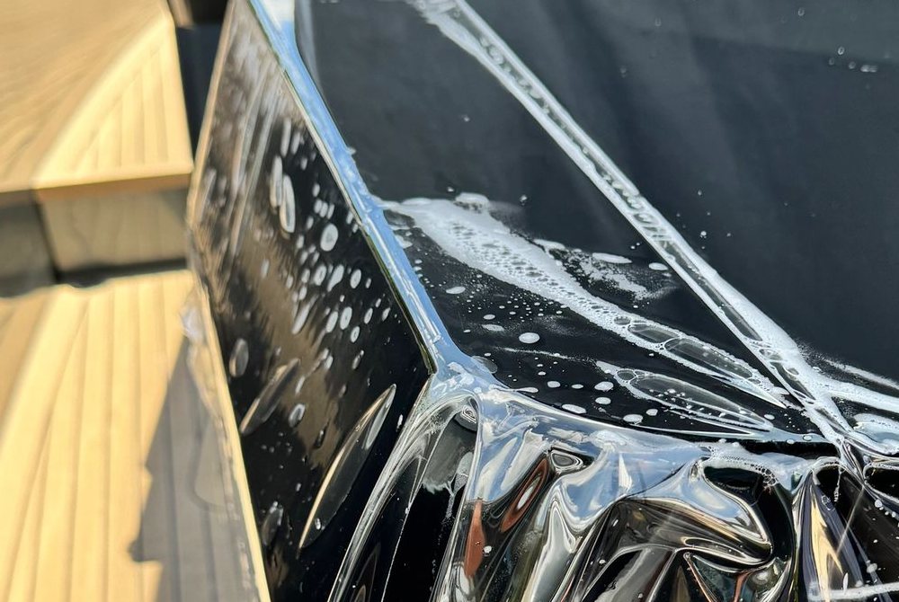 Clear paint protection film being squeegeed across a black gloss yacht surface